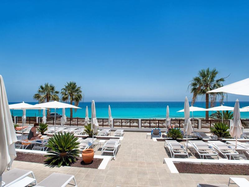 Club de plage moderne avec chaises longues blanches, parasols et vue sur la mer bleue
