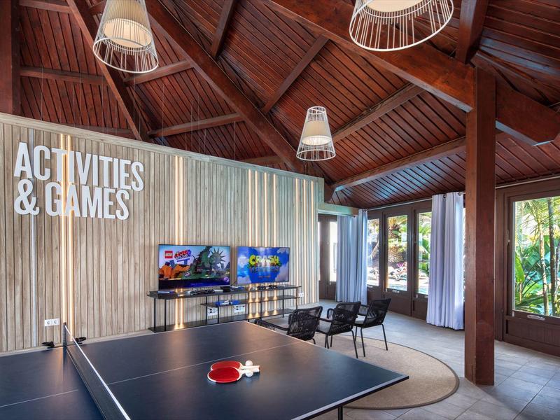 Salle d'activités moderne avec table de ping-pong, jeux d'arcade et plafond en bois dans un hôtel.