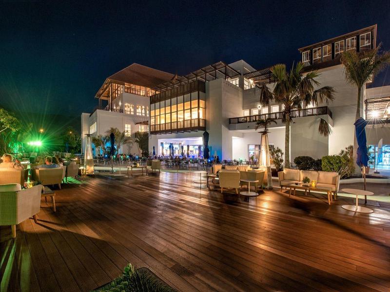Terrasse d'hôtel moderne la nuit avec sol en bois, espaces de sièges et chauffages éclairés.
