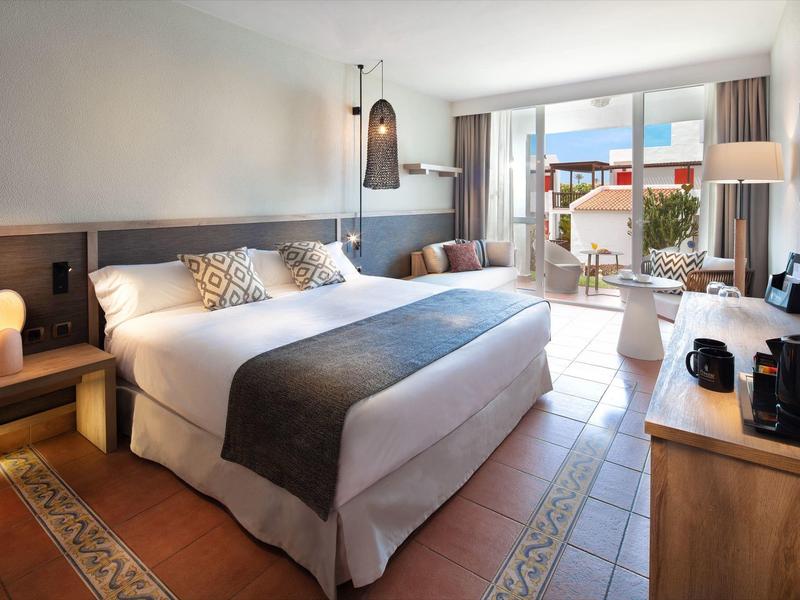 Chambre d'hôtel lumineuse avec grand lit, coin salon et balcon avec vue.