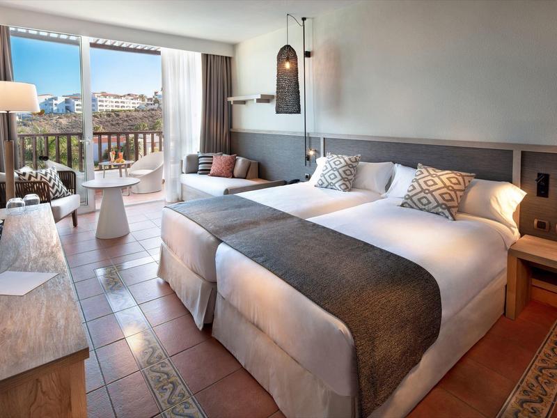 Chambre d'hôtel lumineuse avec lit double, décoration moderne et balcon avec vue sur la ville.