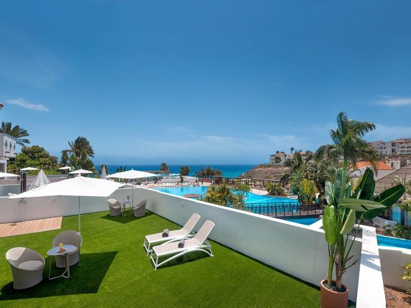 Vue d'une terrasse avec des chaises longues, des plantes et la mer en arrière-plan par ciel clair.
