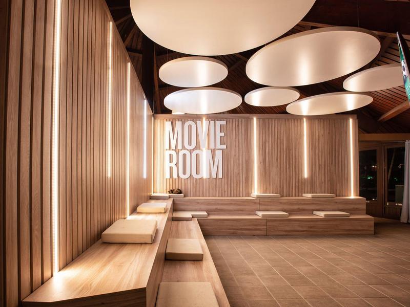 Espace d'attente moderne avec panneaux en bois et grandes lumières ovales au plafond dans la salle de cinéma.