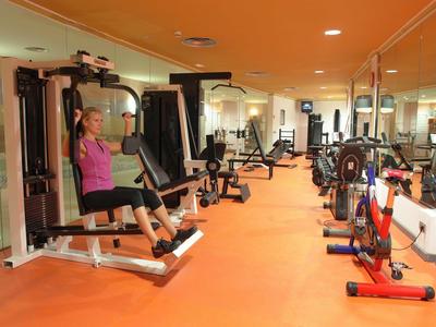 Modernes Fitnessstudio mit orangem Boden, Spiegelwand und verschiedenen Trainingsgeräten.