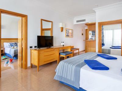 Helles Schlafzimmer mit großem Bett, blau-weißer Bettwäsche, Holzmöbeln und Spiegeln an der Wand.