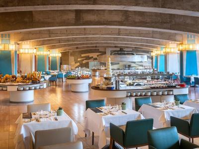 Großer, heller Speisesaal mit runden Buffets, weißen Tischtüchern und blauen Stühlen.