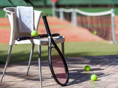 Tennisschläger lehnt an Stuhl mit Handtuch, Tennisbälle liegen auf Boden vor Tennisplatz.