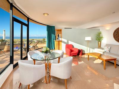 Helles Wohnzimmer mit großen Panoramafenstern, weißem Sofa, rotem Sessel und Meerblick.