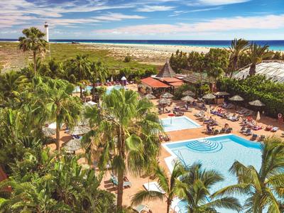 Pohled na hotelový resort s bazény, palmami a lehátky u moře.