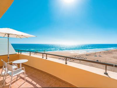 Balkon met stoel en parasol met uitzicht op zonnig strand en zee.