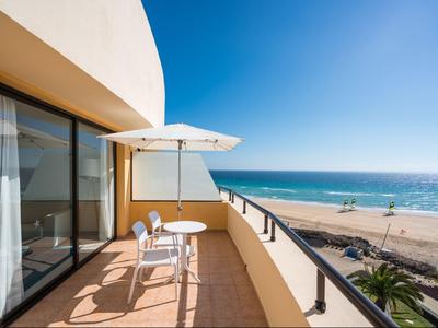 Hotelbalkon met tafel, stoelen en parasol met uitzicht op het strand en de oceaan.