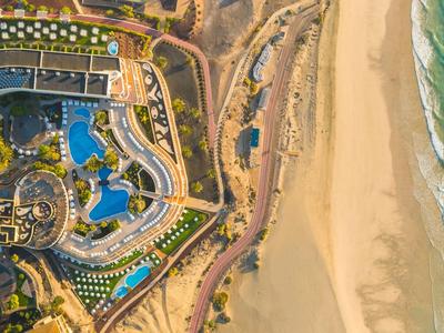Luchtfoto van een resort met zwembaden naast een lang zandstrand en zee.