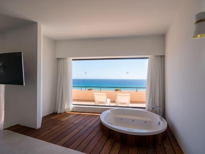 Hotelkamer met jacuzzi op houten terras en zeezicht door panoramisch raam