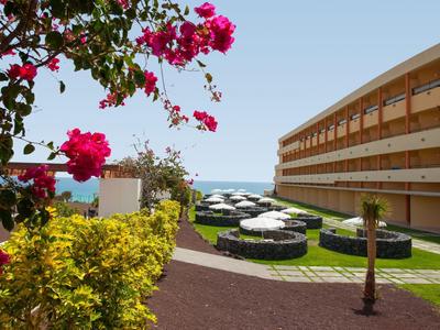 Hotelcomplex met tuin, bloeiende planten en uitzicht op zee op de achtergrond