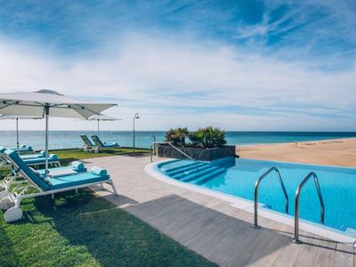 Zwembad met blauwe ligstoelen en witte parasols op het strand onder een blauwe lucht.