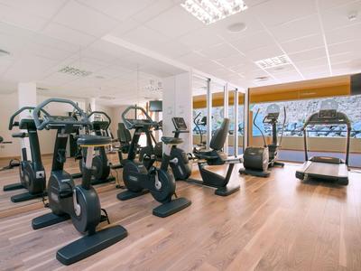 Fitnessruimte met meerdere cardiotoestellen en grote ramen met uitzicht op het water.