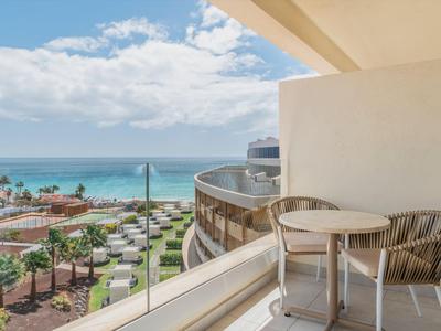 Balkon met tafel en stoelen met uitzicht op zee en tuin in een vakantiehotel.