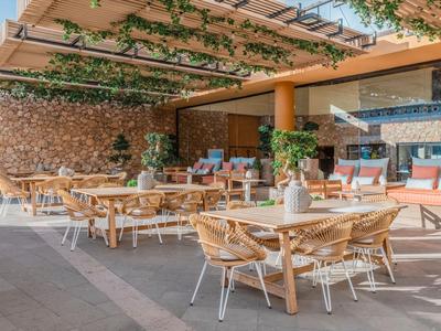Buitenrestaurant met houten en gevlochten stoelen, vazen op tafels en hangende planten.