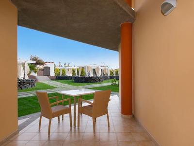 Uitzicht vanaf een terras met tafel en twee stoelen op een groen hotelterrein bij zonnig weer.