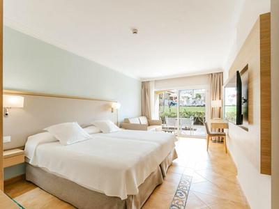 Bright hotel room with two single beds and view of a terrace with garden.