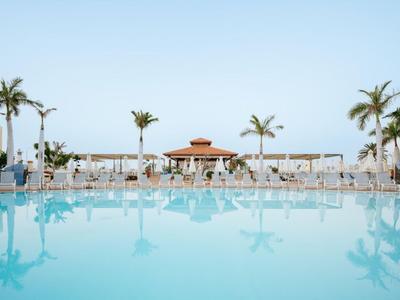 Large pool with clear water, lounge chairs, and palm trees under a clear sky