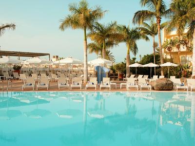 Clear swimming pool with sun loungers and palm trees under sunny sky.