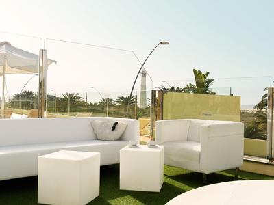 Modern white outdoor furniture on terrace with glass railing and view of plants.