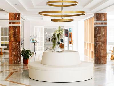 Bright hotel lobby with white round sofa and modern gold ceiling lights.