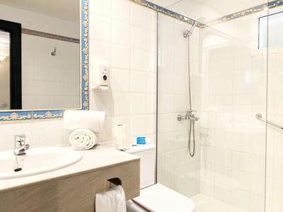 Bright bathroom with sink, mirror, toilet, and walk-in shower with glass partition.