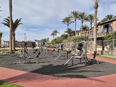 Outdoor-Fitnessbereich mit Calisthenics-Geräten, umgeben von Palmen und Hotelgebäuden.