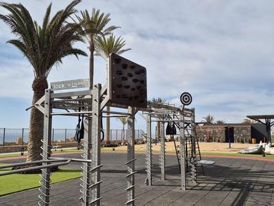Moderner Außen-Spielplatz mit Klettergerüst, umgeben von Palmen und Meerblick.