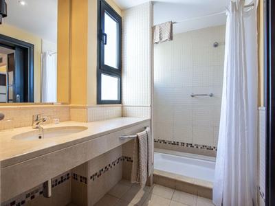 Salle de bain lumineuse avec lavabo, grand miroir et cabine de douche avec rideau.