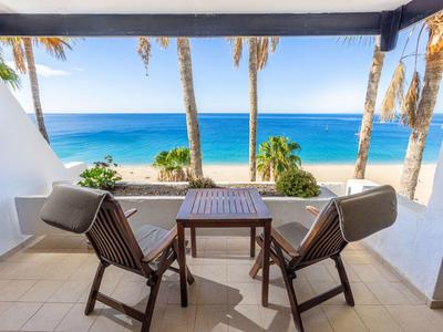 Balcon avec deux chaises et une table avec vue sur les palmiers et la mer.