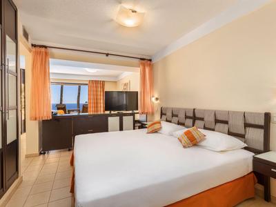 Chambre d'hôtel lumineuse avec lit double, rideaux orange et vue sur la mer.