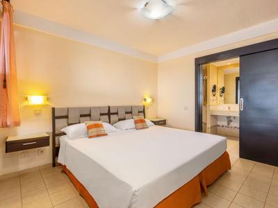 Chambre d'hôtel lumineuse avec un grand lit double, des tables de chevet et accès à la salle de bains.