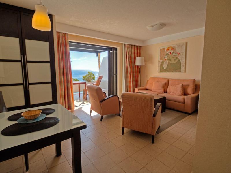 Světý obývací pokoj s pohovkou, křesly a přístupem na balkon s výhledem na moře.