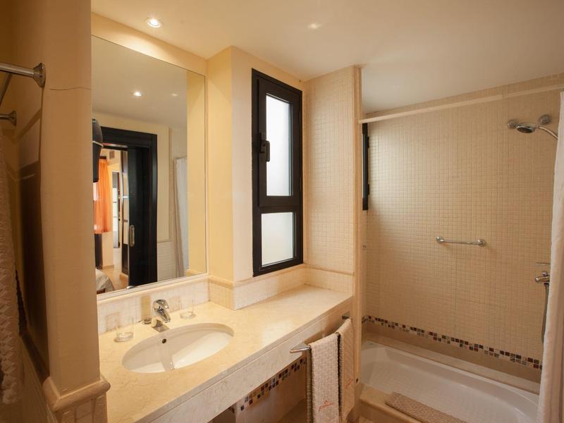 Světla hotelová koupelna se umyvadlem, zrcadlem, ručníky a sprchou se závěsem.