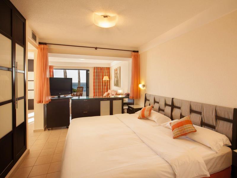 Světý hotelový pokoj se dvěma postelemi, TV a přístupem na balkon.