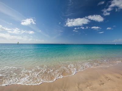 Clear blue sea and sky with sandy beach under bright sunlight.