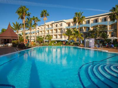 Hotel con piscina grande, palmeras y terraza soleada bajo cielo despejado