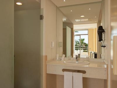Bright hotel bathroom area with sink, mirror, and separate shower stall