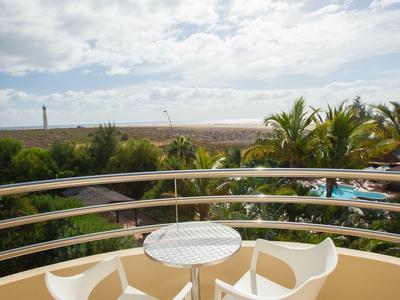 Balcony with three white chairs and small table overlooking the sea and palm trees.