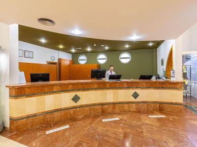 Moderne Hotelrezeption mit einem gebogenen Holztresen und einem Mitarbeiter hinter dem Schalter.