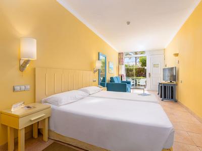 Helles Hotelzimmer mit großem Bett, gelben Wänden und Sitzbereich am Fenster.