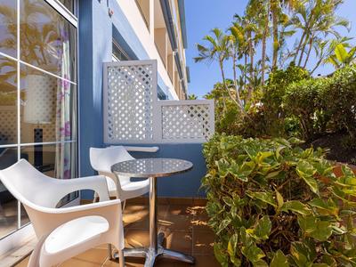 Kleiner Balkon mit weißen Stühlen, rundem Tisch und Pflanzen bei Sonnenschein.