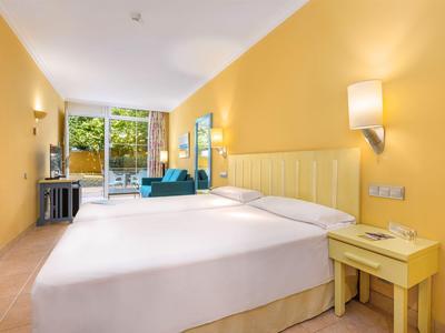 Helles Hotelzimmer mit großem Bett, gelben Wänden und balkon mit Blick ins Grüne.