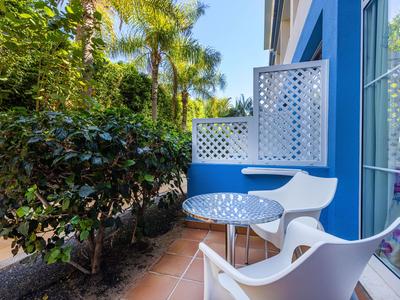 Balkon mit blauem Wand, zwei weißen Stühlen und einem runden Tisch neben Pflanzen.