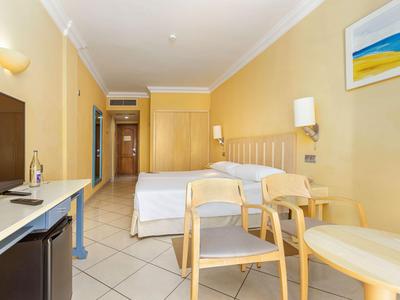 Helles Hotelzimmer mit Doppelbett, Holzmöbeln und einem Wandbild über dem Bett.