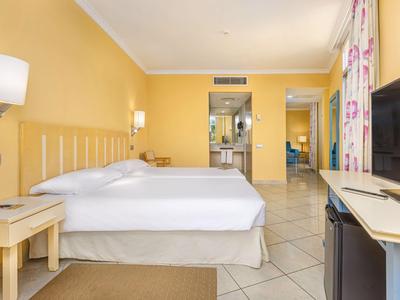 Helles Hotelzimmer mit zwei Betten, gelben Wänden und Fliesenboden.