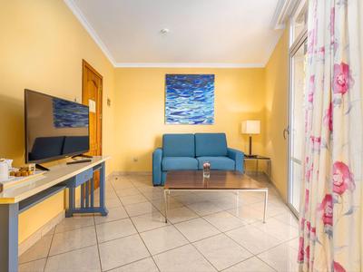 Wohnzimmer mit blauer Couch, großem Flachbildfernseher und gelben Wänden.